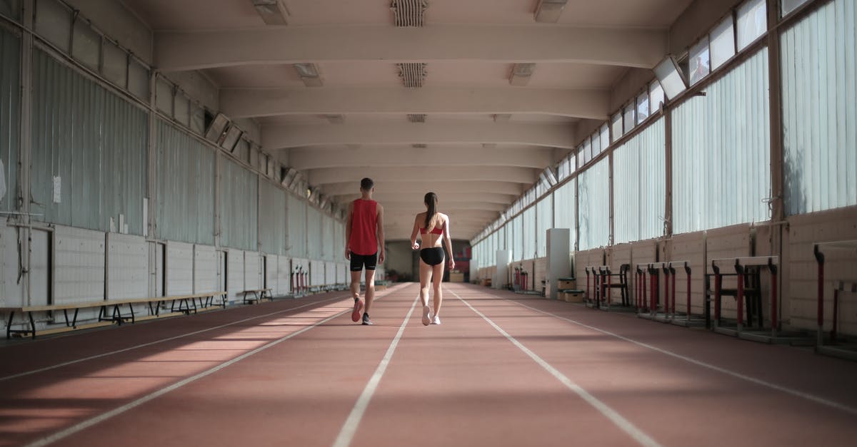 What happens when the arena timer runs out? - Back view of sportsman and sportswoman in activewear walking along running track in athletics arena during warming up before training