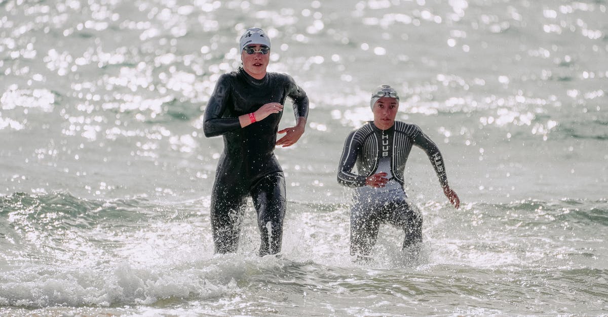 What happens when your Stamina/Psyche Meter runs out? - Focused young people in wet suits and swim caps running out of wavy glistening sea in sunlight