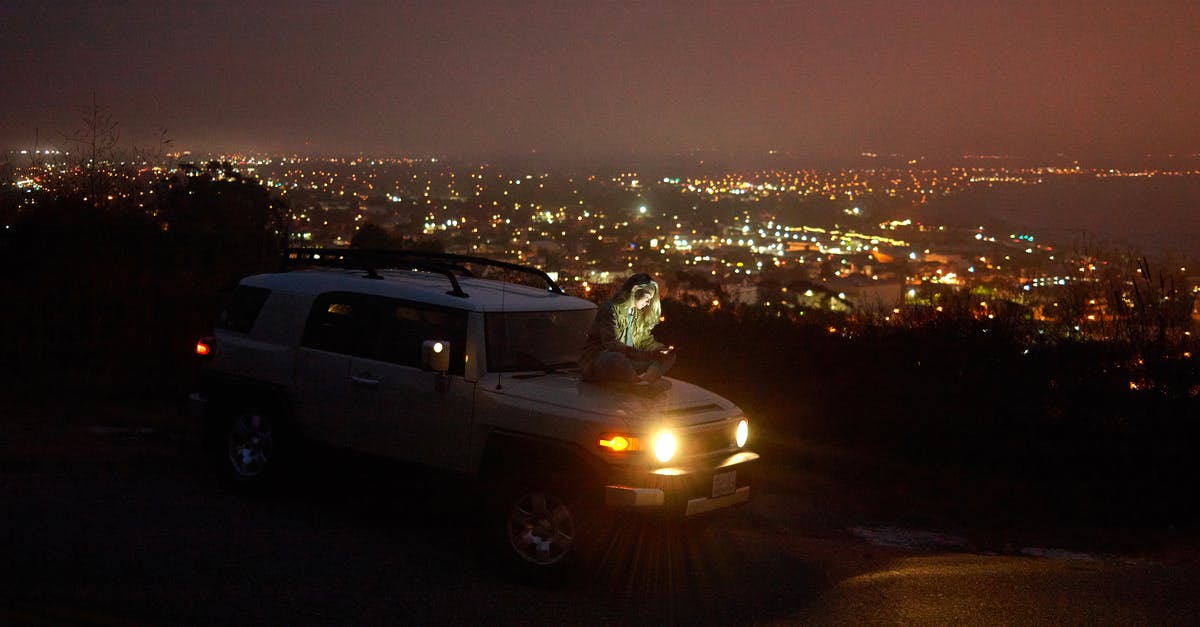 What is the fastest SUV in GTA online? - Young pensive woman sitting on hood of car and messaging on smartphone against cityscape at night