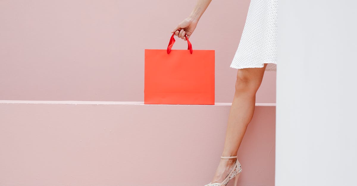 What is there to spend my rupees on? - Crop anonymous stylish female in white dress and high heels carrying red shopping bag against pink wall