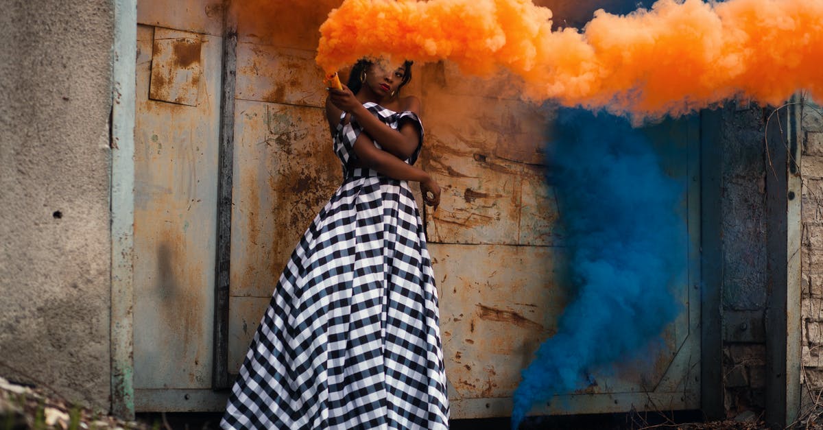 What is this blue smoke behind a wall? - Woman in White and Black Dress Holding Orange Smoke