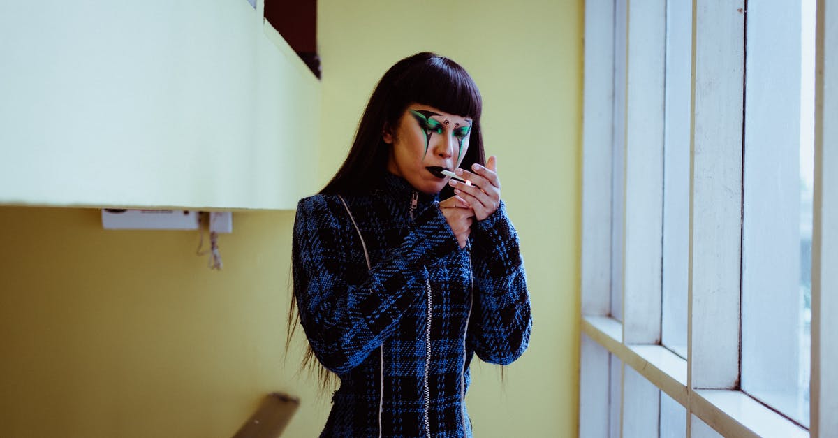 What is this blue smoke behind a wall? - Stylish Asian woman with body art on face cigarette near window