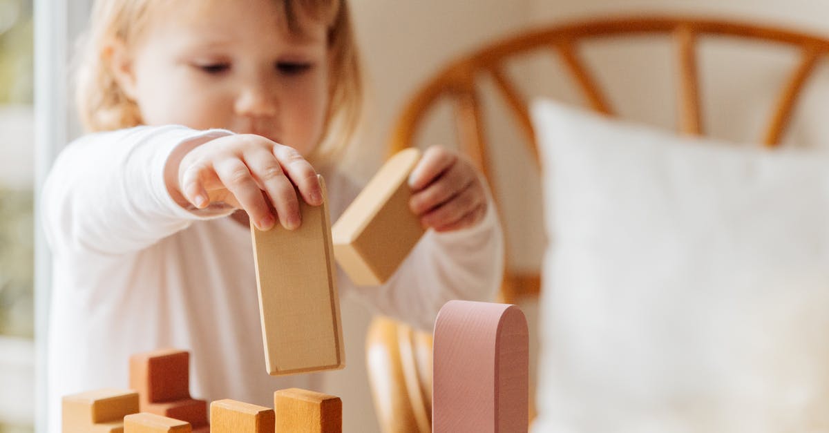 What is this small Nintendo-branded stand for? - Cute little girl in white casual clothes standing near table and playing with wooden blocks while spending time at home