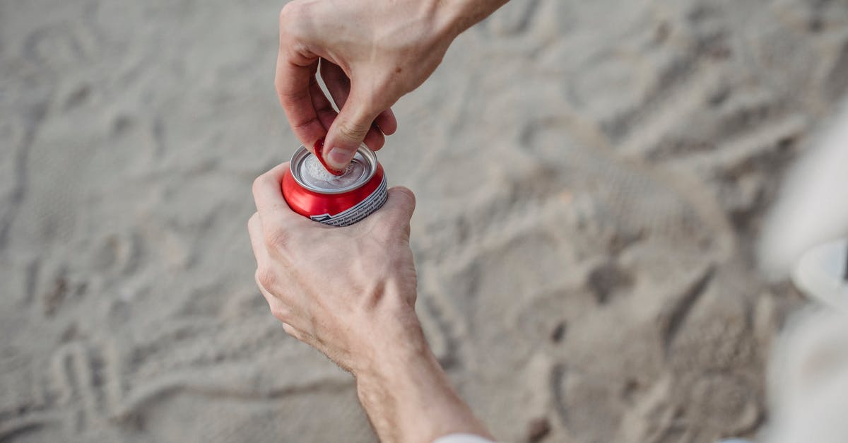 What metals can be extracted from what items? - From above of crop anonymous male opening can of drink standing on sandy beach