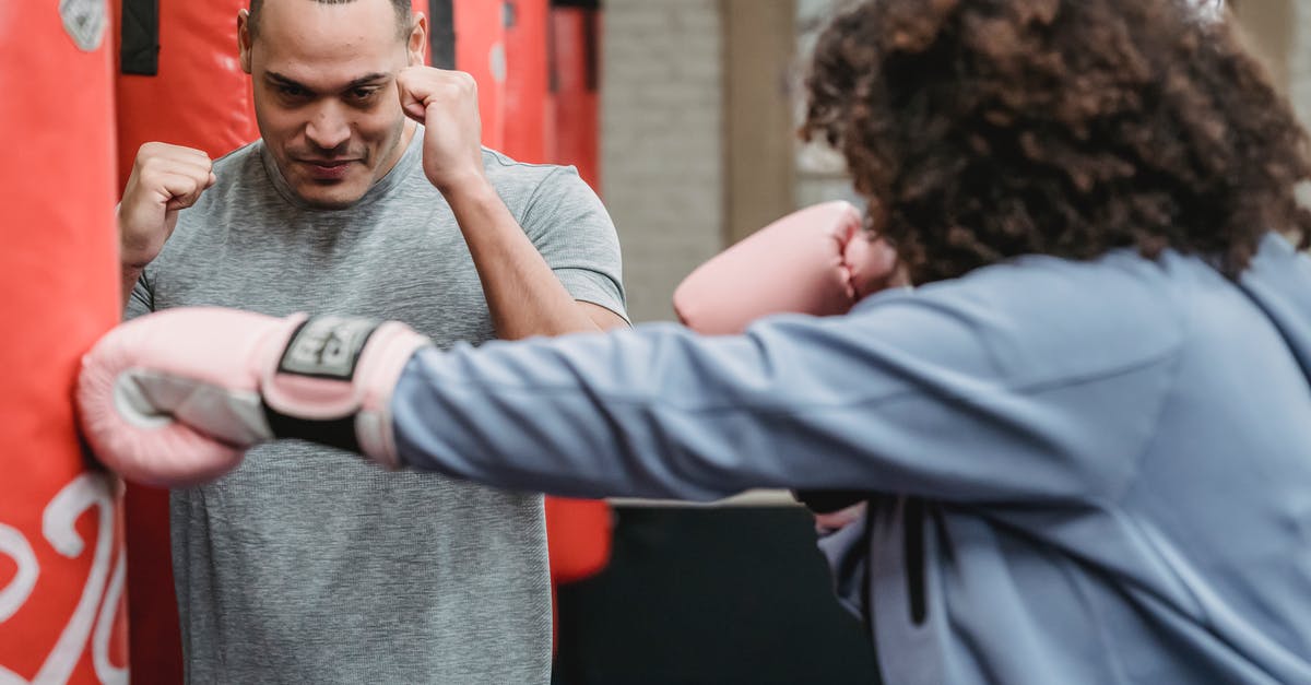 What triggers a multiple hit attack? - Serious ethnic male instructor showing boxing stance to female in gloves hitting punching bag during workout