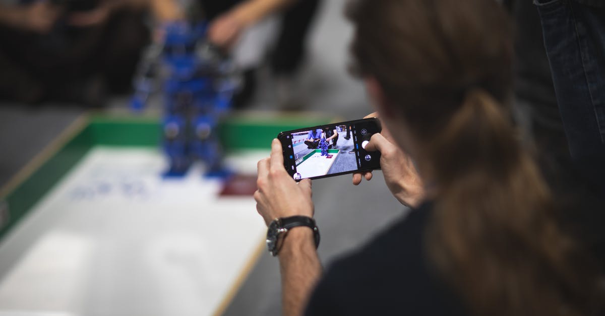 When using a capture card, where is my game displayed? - Back view of male photographer with ponytail in casual clothes shooting video of robot testing on mobile phone in modern studio