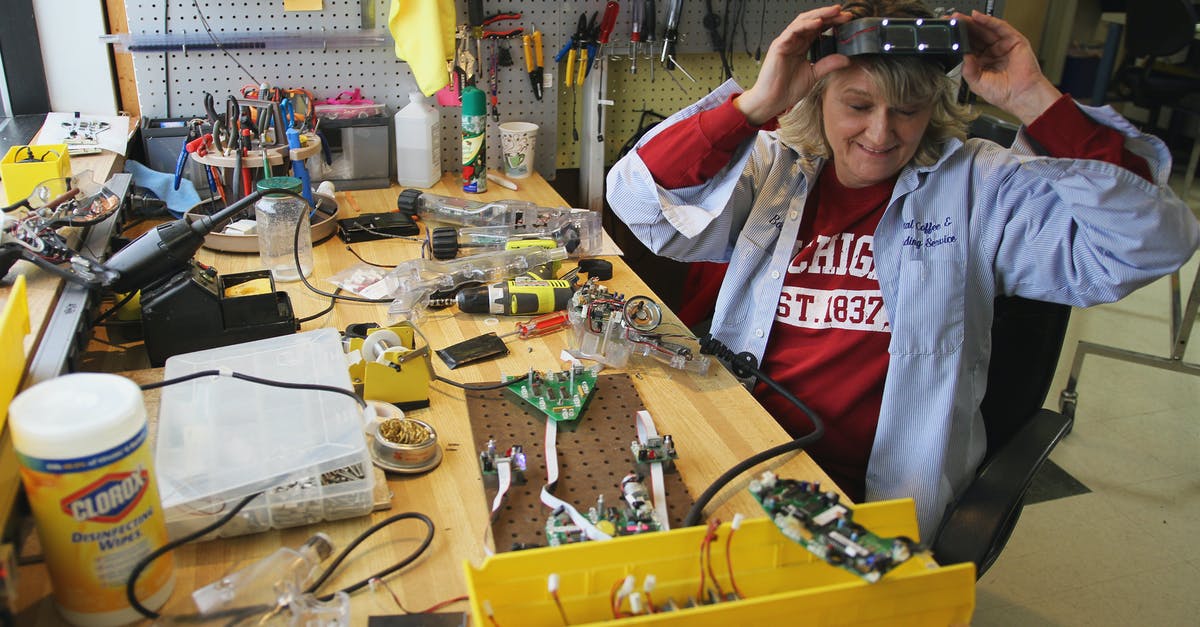 Where do the plastic boxes for screw containers come from? - From above of cheerful female worker in headband magnifier glasses sitting at table with assorted tools and microchips while looking down