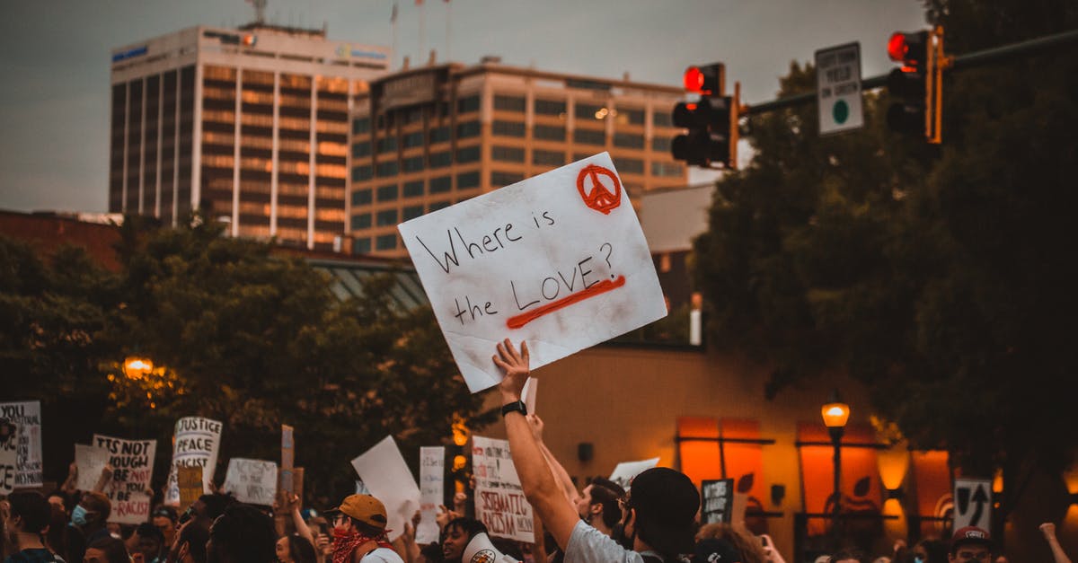 Where is the Benefactor? - Multiracial people with banners protesting on street in evening