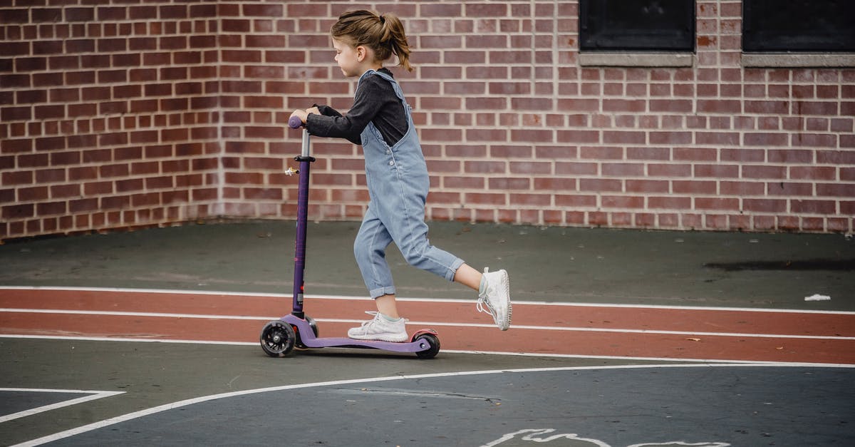 Which heroes move the fastest along the ground? - Side view of excited preschool girl in casual outfit riding scooter on asphalt sports ground