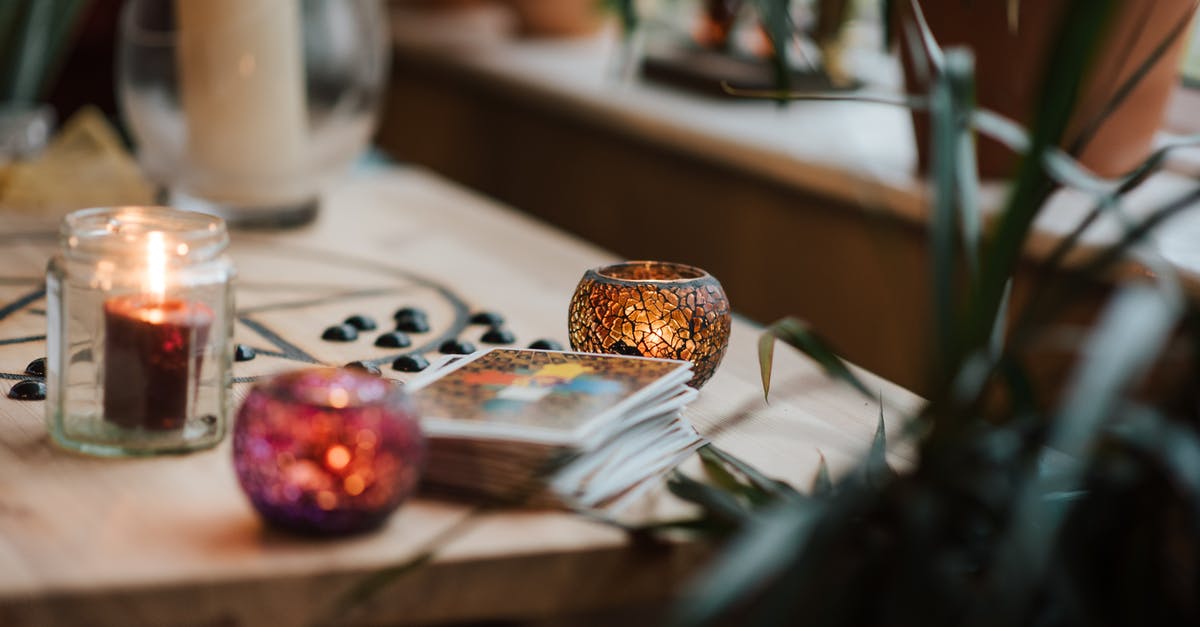 Which items have the highest enchantment values? - Luminous candles in holders near tarot cards on table with oracle symbol at home