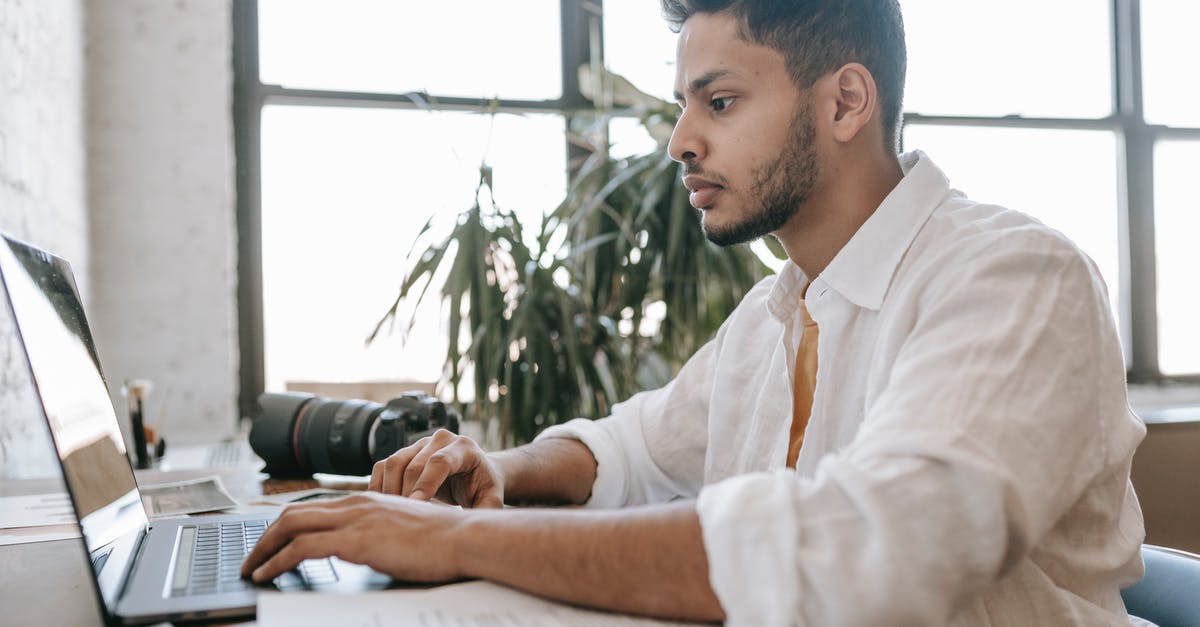 Why can't I edit or create my sim? - Side view attentive young ethnic male photographer wearing white shirt editing photos on modern netbook while sitting at desk with professional photo camera