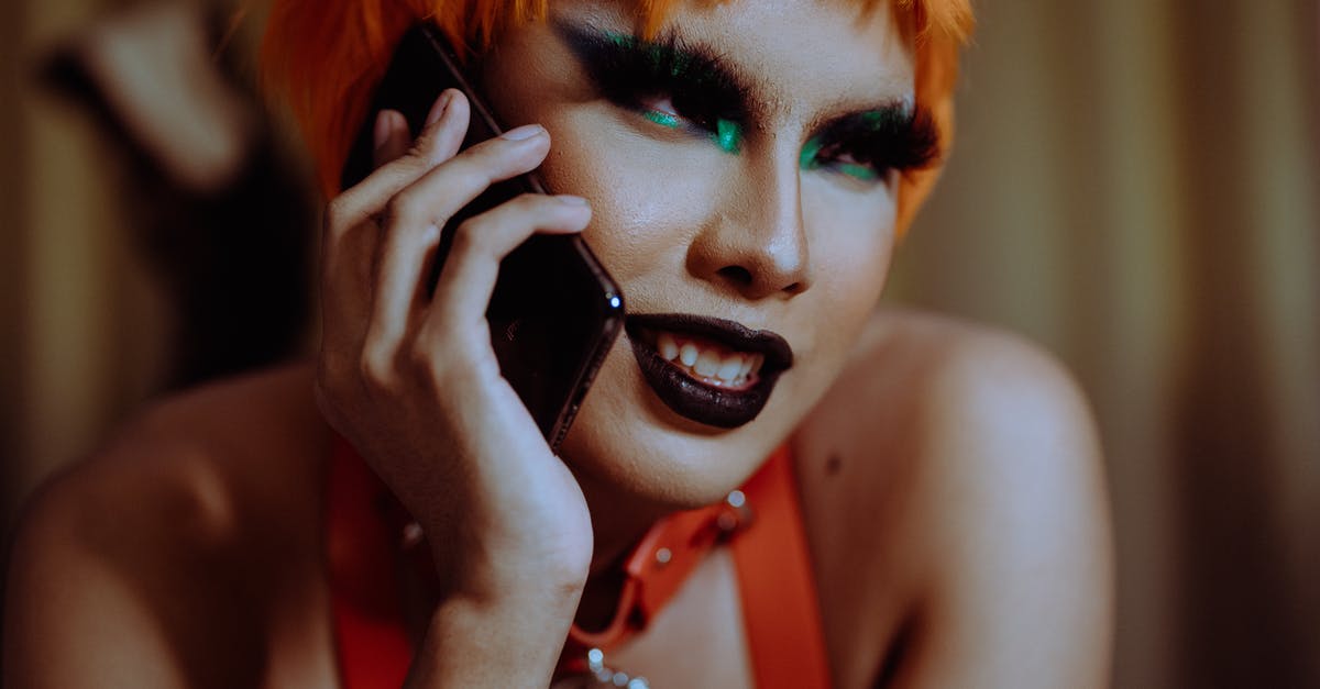 Why can't I talk to this character anymore? - Crop young informal ethnic lady with bright makeup and short orange hair smiling while lying on stomach and talking on smartphone