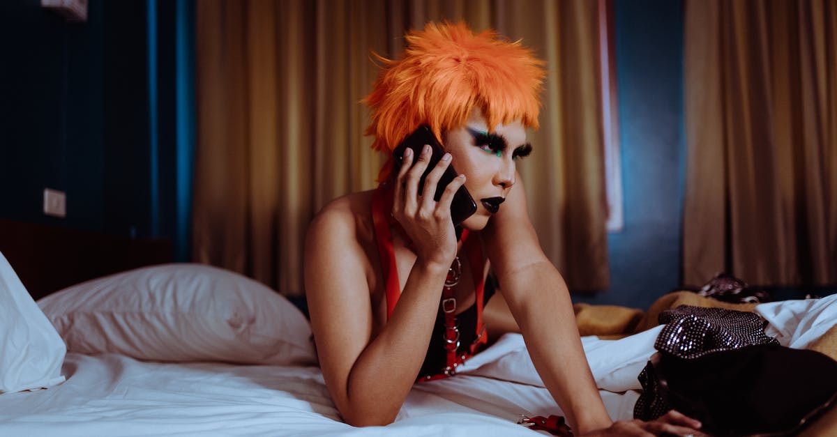 Why can't I talk to this character anymore? - Seductive young ethnic female with makeup in orange wig lying on bed and chatting on mobile phone