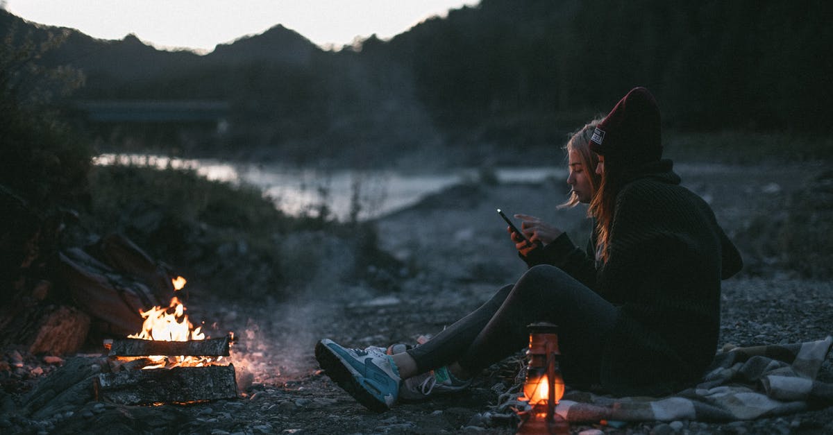 Why can't I use Fire Bombs? - Side view of young girlfriends resting on shore of river near campfire while using smartphone in evening