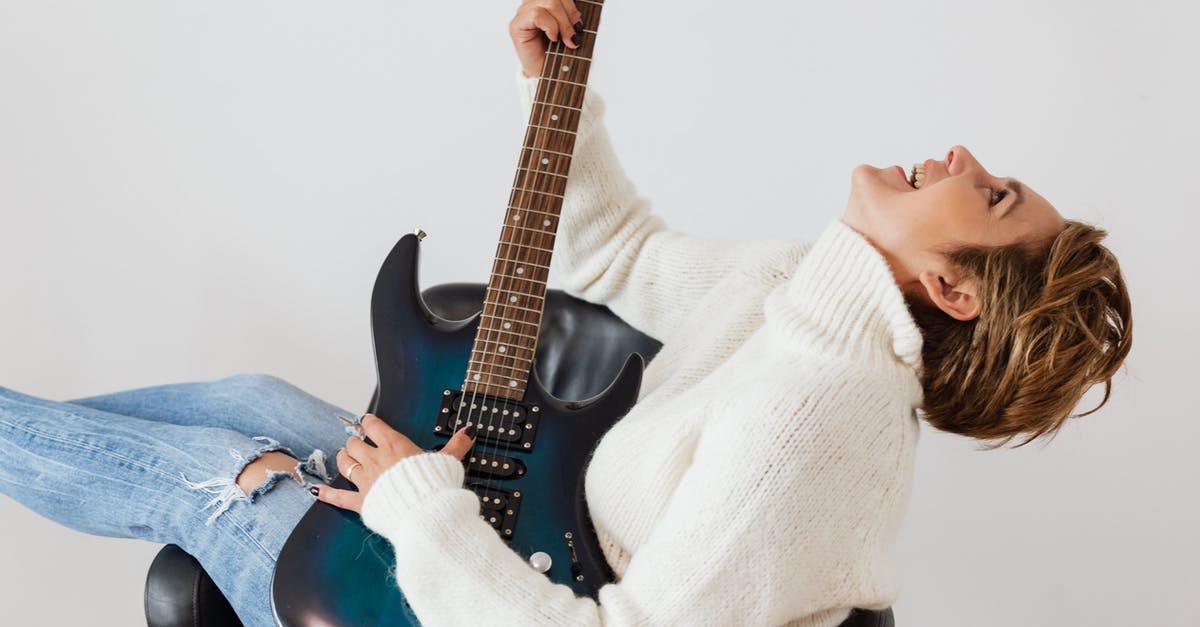 Why do I have staticy sound? - Side view of cheerful short haired female in casual clothes laughing while playing electric guitar in comfortable armchair against white background