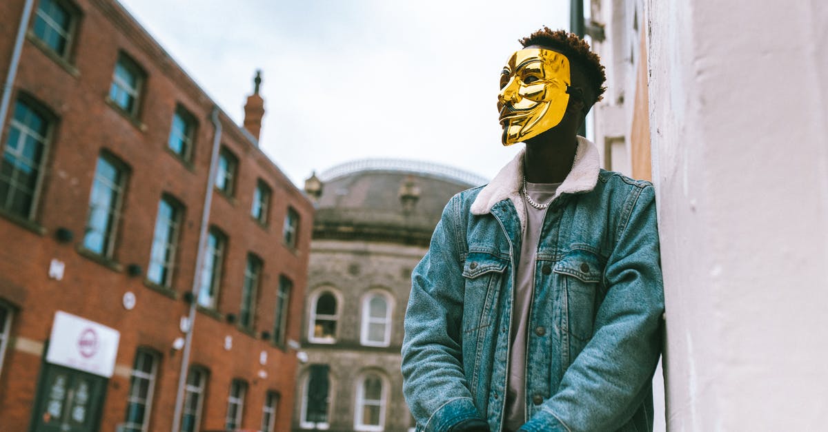 Why is my social policy cost so high? - From below of confident black activist in stylish outfit and famous Anonymous mask leaning on building placed in city district in daytime