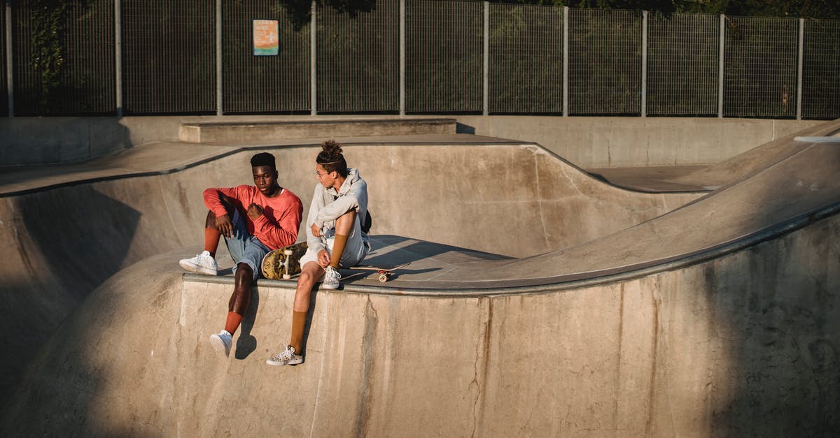 Why is the ability red? - Young diverse male friends spending free time together while sitting with skateboards on ramp in skate park on summer sunny day