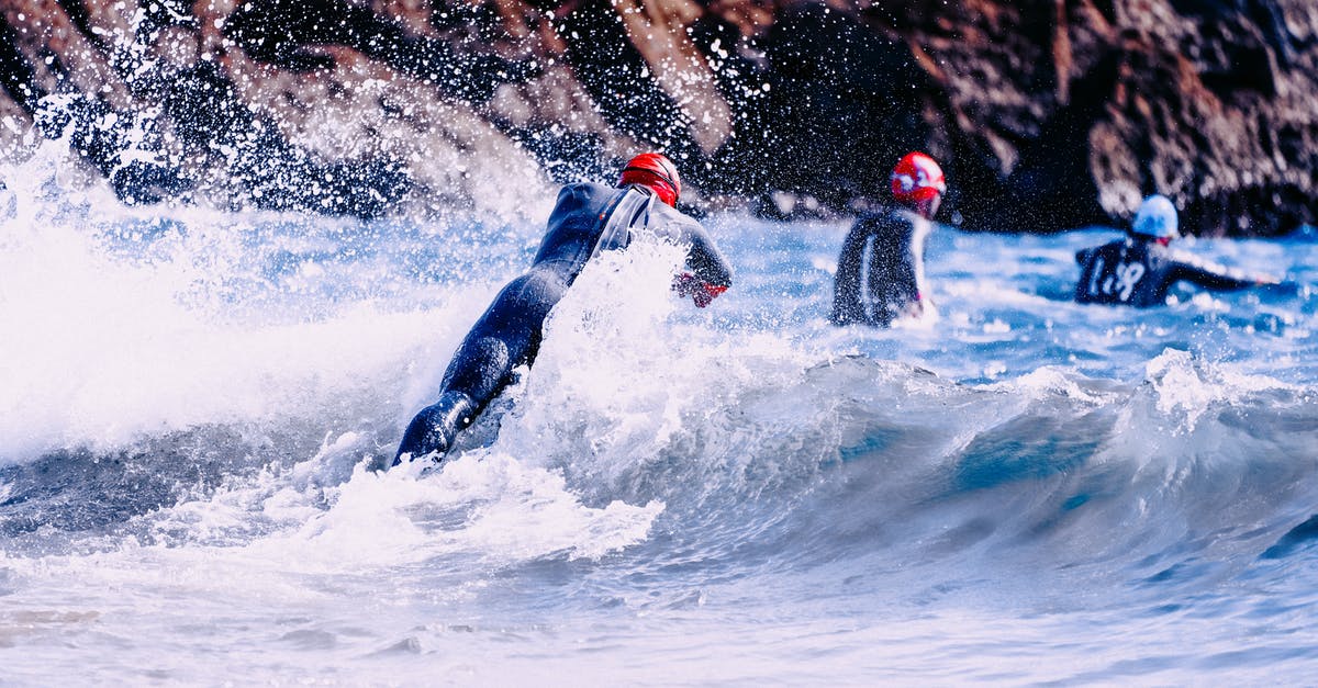 Why is the dive on Another Day missing? - Group of faceless sportspeople in suit for bathing and swim caps jumping into azure wavy sea near steep mountain in sunlight