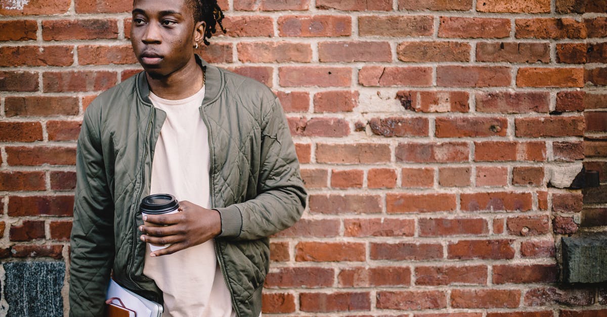 Why won't this wall break? - Pensive young man with coffee and notebooks standing near wall