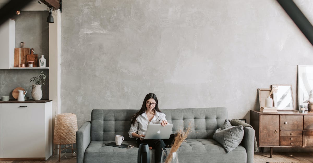 Why won't this wall break? - Happy female remote worker in eyeglasses sitting on cozy sofa with netbook and cup of coffee in loft style room with wooden floor and concrete wall