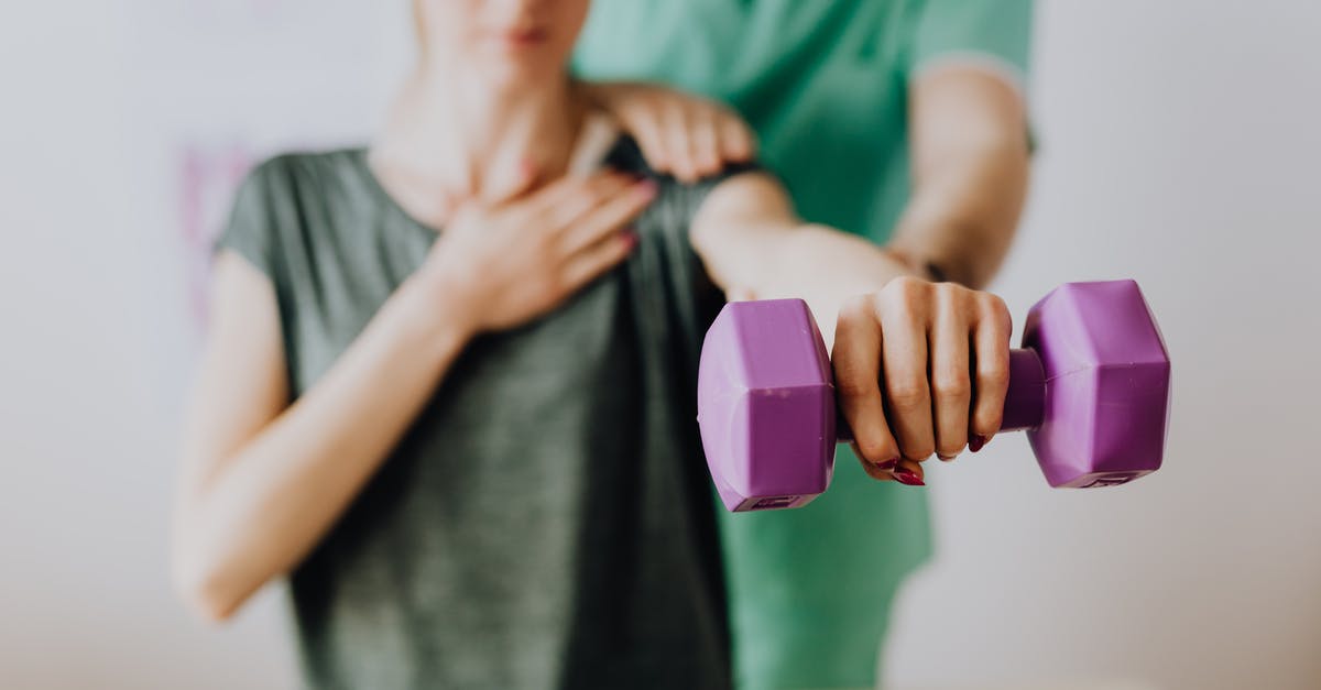 Wilken's Reach and Zunimassas - Crop unrecognizable orthopedist in uniform helping slender female in casual wear reaching arm with dumbbell in doctor office in hospital