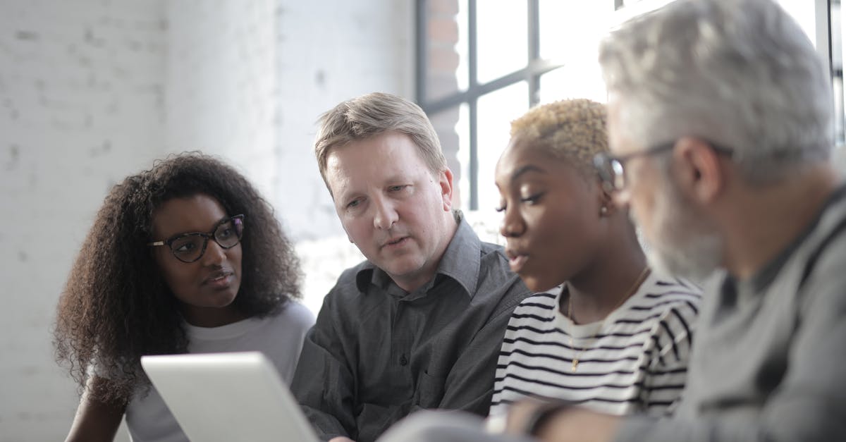 Zodiac Age - What to consider when choosing job combinations? - Group of focused multiethnic coworkers in casual clothes watching portable computer screen while sitting near fenced window behind brick wall in sunlight